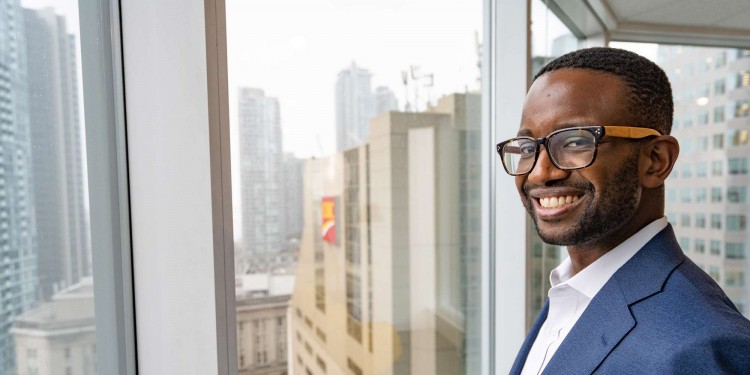 Image of Matthew Colphon standing in front of a high-rise office window with buildings in the background