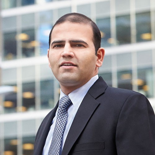 Image of Alumni student, Varun Sharma, in a business suit standing outside of a building