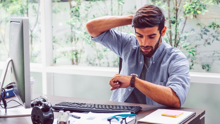 A businessman checking the time on his watch while sitting at a desk.